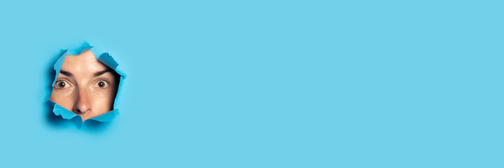 Woman peeps and looks out of the hole on a blue background. Listen, spy, wiretapping