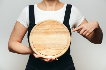 Woman in apron pointing finger to black cutting board.