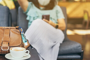 Mini alcohol gel bottle to kill Corona Virus(Covid-19) hang on a brown leather shoulder bag with hot coffee on table in cafe.New normal lifestyle.Health care concept.Selective focus on alcohol gel