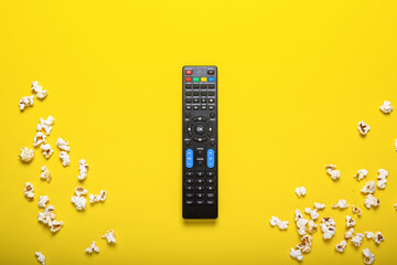 Black remote control from a TV, TV tuner or audio system on a yellow background with popcorn. Concept TV series, film, sports. Flat lay, top view