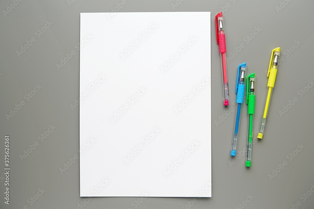 Wall mural White empty paper sheet, colorful gel pens on grey background, coloring page, planner mockup, back to school concept.