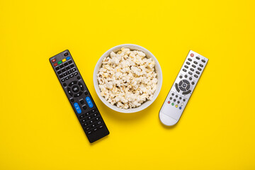 Two remotes from the TV, TV tuner and a bowl of popcorn on a yellow background. Concept series, film, sports. Banner. Flat lay, top view