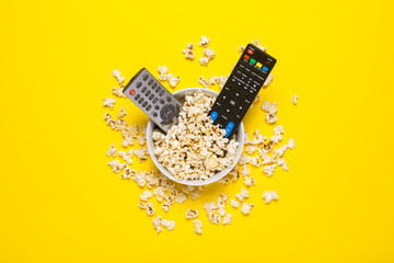 Two remotes from the TV, TV tuner lie in a bowl with popcorn on a yellow background. Concept series, film, sports. Banner. Flat lay, top view