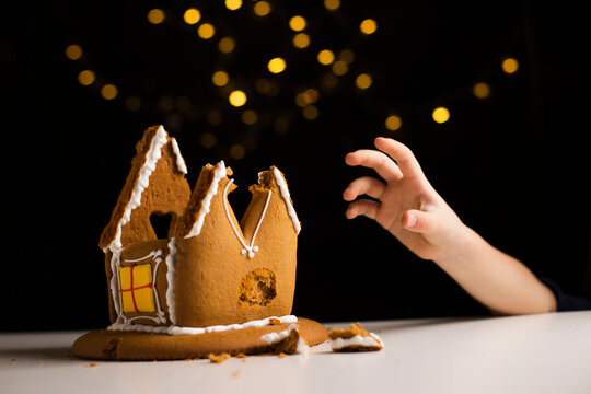 Young boy hand reaching gingerbread house leftovers on table. Delicious biscuit dessert remains