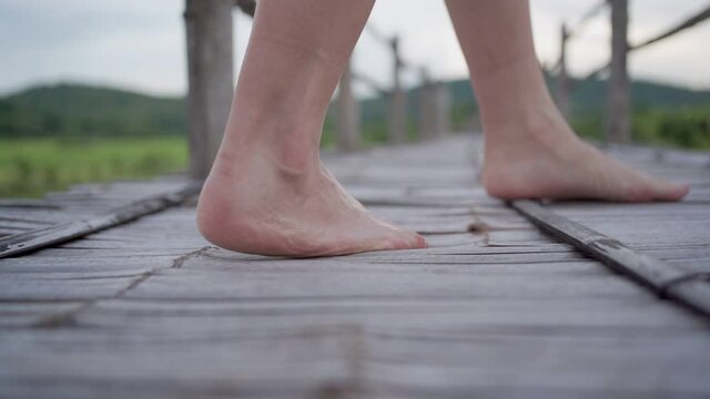 slow motion close up female  bare feet on walking  wood bridge, with green rice field and mountain on the background, non urban scene touch the local nature, human health wellness, retreat peaceful