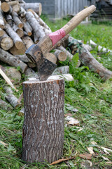 Ax in a stump against the background of a pile of firewood in a village yard.