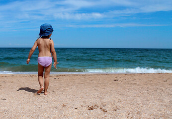 A little girl in a blue Panama hat looks at the sea and the clear blue sky. The concept of a comfortable holiday at the sea, a happy childhood, good memories.