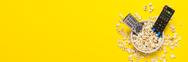 Two remotes from the TV, TV tuner lie in a bowl with popcorn on a yellow background. Concept series, film, sports. Banner. Flat lay, top view
