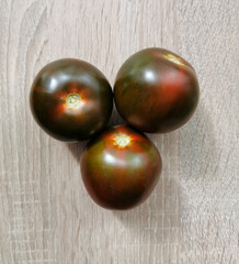 Three fresh, dark red heirloom tomatoes on a wooden table.