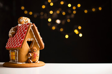 Beautiful idyllic gingerbread house with red roof icing, dark background with fairy lights, copy space