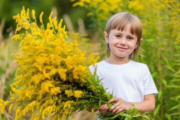 A little girl in the flower field, holds a bouquet of yellow flowers and smiles.
