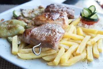 Delicious dish from Bosnian cuisine - mixed meat skewers served with french fries, grilled vegetables and rice with paprika 
