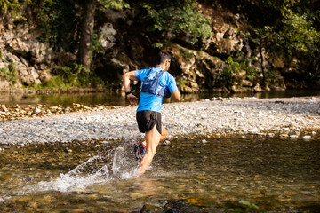 Young man in sports equipment running in mountain river 