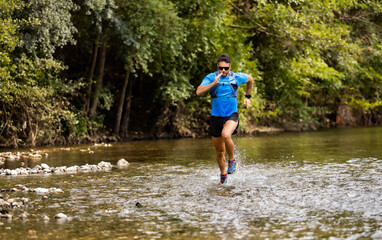 Fototapeta na wymiar Young man in sports equipment running in mountain river 