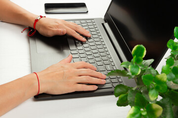female hands are typing text on laptop keyboard on white wooden table background