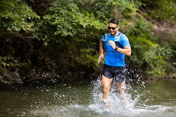 Young man in sports equipment running in mountain river 