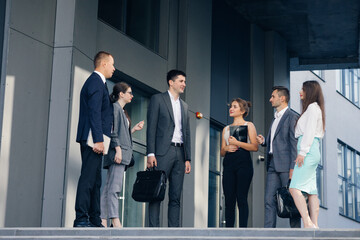 Confident team members on stairs. Business men and women in formal suits talk on the background of modern office building. Male and Female Business People Discuss Business. Group of six people.