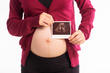 Close up of pregnant woman standing and posing while showing ultrasound scans on a white background.  .