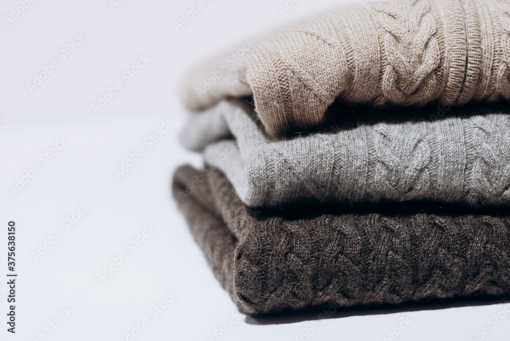 Wall mural Three folded cashmere knitted sweaters in different shades of gray on white background. three shades of gray. Stack of three sweaters isolated on black background. Knitted wool sweaters.