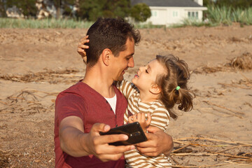 little happy daughter hugs daddy selfie on beach on sunny day