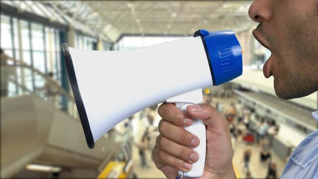 Close up african-american man talking into megaphone. Underground subway background with moving escalator in the background.