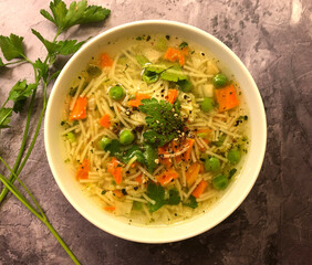 Vegetable soup with carrot, green peas, noodles and parsley on stone background.
