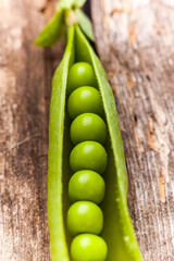 open pod of green peas on a wooden table close-up