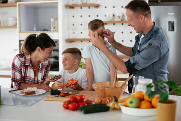  Mother and father making breakfast with sons. Young family preparing delicious food in kitchen.