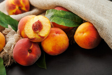 Peaches on a black background with burlap fabric and green leaves. Sweet and juicy peach slices with a stone
