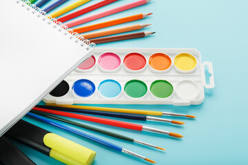 An album of brushes and paints with school supplies on a blue background. Album, a place to copy space.