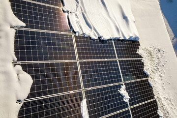 Close up surface of a house roof covered with solar panels in winter with snow on top. Energy efficiency and maintenance concept.