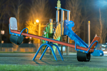 Seesaw swing in preschool yard with soft rubber flooring at night. - obrazy, fototapety, plakaty