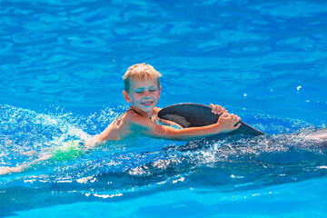 Happy little boy swimming with dolphins in Dolphinarium
