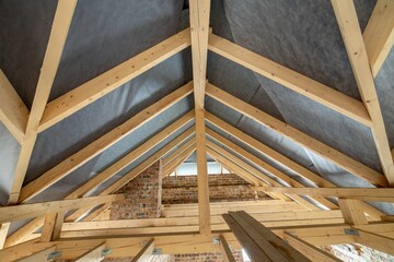 Obraz premium Attic space of a building under construction with wooden beams of a roof structure and brick walls. Real estate development concept.