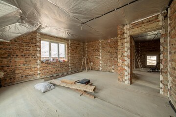 Interior of unfinished brick house with concrete floor and bare walls ready for plastering under construction. Real estate development