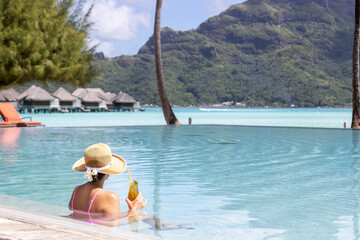 Woman sits in swimming pool holding iced tea glass while on vacation at a tropical island