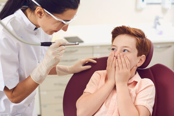 Dental clinic. Scared boy covering mouth with hands near dentist
