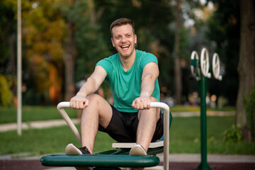 Handsome man training in outdoor gym on rowing machine