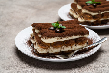 Two portions of Classic tiramisu dessert on ceramic plate on concrete background