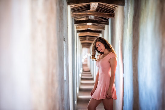 Young woman sexy girl in pink dress side profile standing looking through window of wall of fortress tunnel passage in Castiglione del Lago in Italy