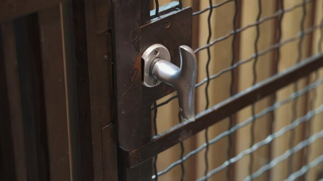 Close up of old vintage elevator going up and arriving at floor. A hand opens door knob and wooden gate