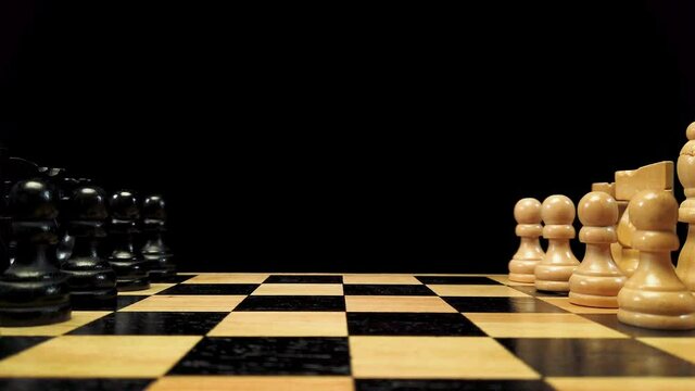 Dolly shot forward along chess pieces standing on either side of a chessboard against a black background.
