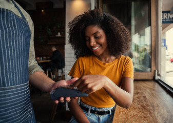 Smiling mixed race woman with afro happily paying for coffee at coffee shop.
