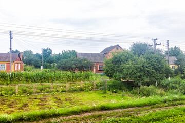 Western Ukraine countryside village with view through train window of outdoor park garden in summer and old dacha cottage with green plants and power lines