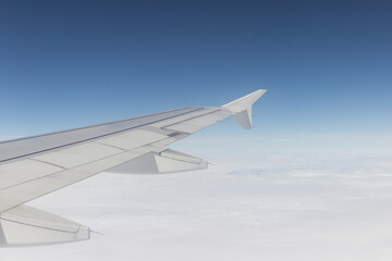 wing of an airplane that is in the air, the sky is clear with clouds in the day