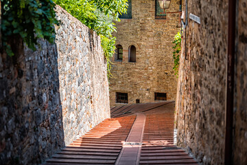 Fototapeta na wymiar San Gimignano, Italy small historic medieval town village in Tuscany with view narrow street alley and stone steps on sunny day in summer