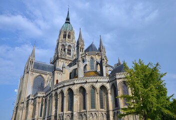 Cathedral Notre-Dame in the town of Bayeux in the county of Calvados in Normandy, France, tree on the right in front, blue sky with clouds background, summer