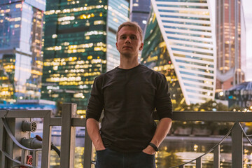 Portrait of a business man in a black sweater with a view of the night illumination business skyscrapers in Moscow