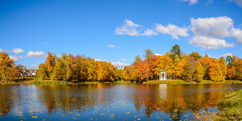 Fototapeta na wymiar Autumn landscape with a pond in the foreground against blue sky