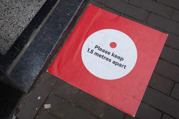 Red sticker on pavement 'Please keep 1.5 meter apart' in front of the threshold at the entrance of...